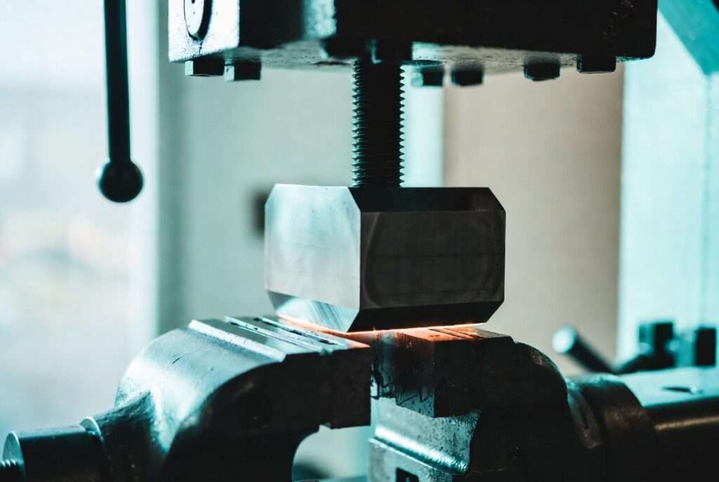 A glowing metallic geometric cube being compressed by an industrial vice, representing the heavy operational friction of the 13 frequency